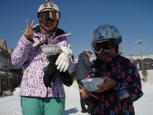 スキーウエアを着てゴーグルをして箸とキノコ汁のお椀をもっている親子の写真