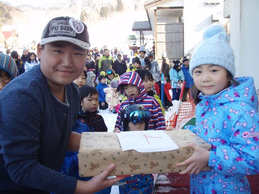 抽選会で当選した商品を抱えている男の子と女の子、その後ろに抽選会に集まった大勢のスキー客が写っている写真