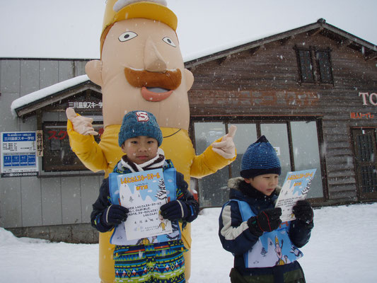 「レルヒさんスキースクール修了証」もって立っている2人の子供とレルヒさんの写真